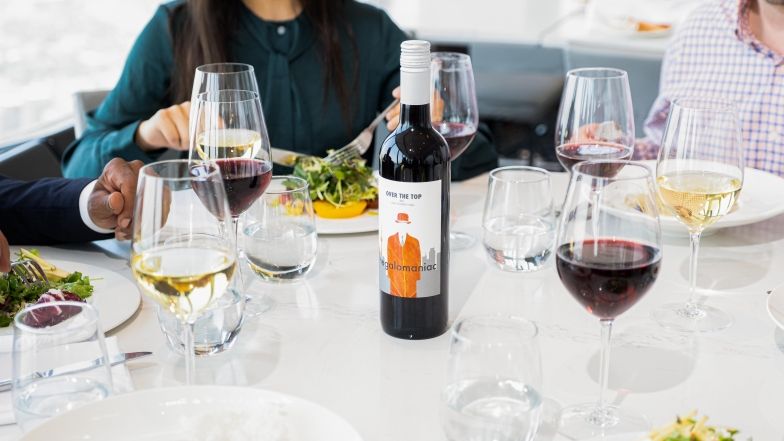 Group sitting at a table at 360. Table is made of white marble and round, filled with wine glasses and food plates. There's a bottle of 360 red wine at the center of the table.