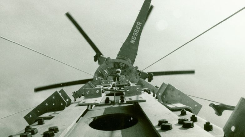 An older photo showing an helicopter above the tower. A person is at the top of the tower.