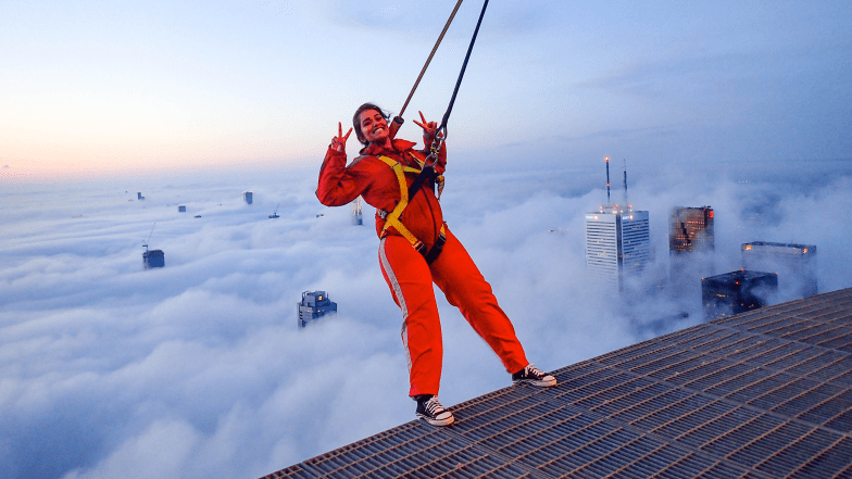 Person in harness leaning backwards over the edge walk. Clouds are below.