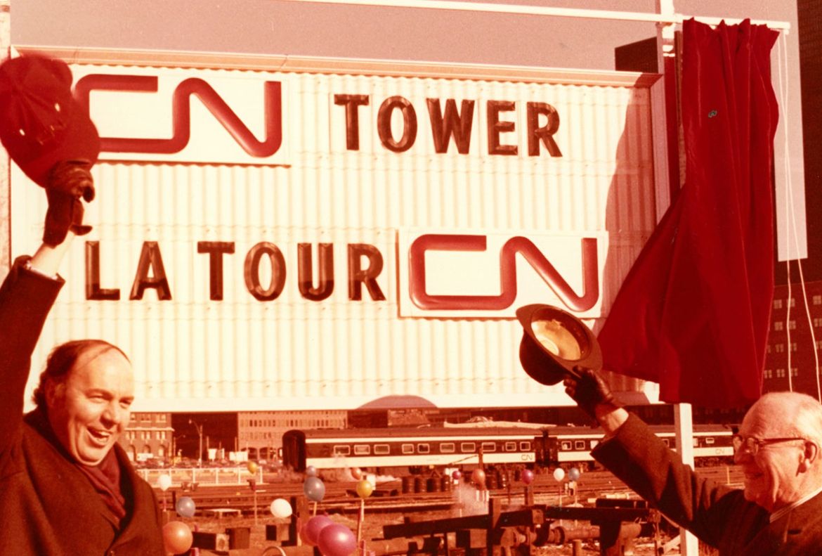 Two men wave their hats at a sign saying “CN Tower” to mark the beginning of the Tower’s construction in February 1973.