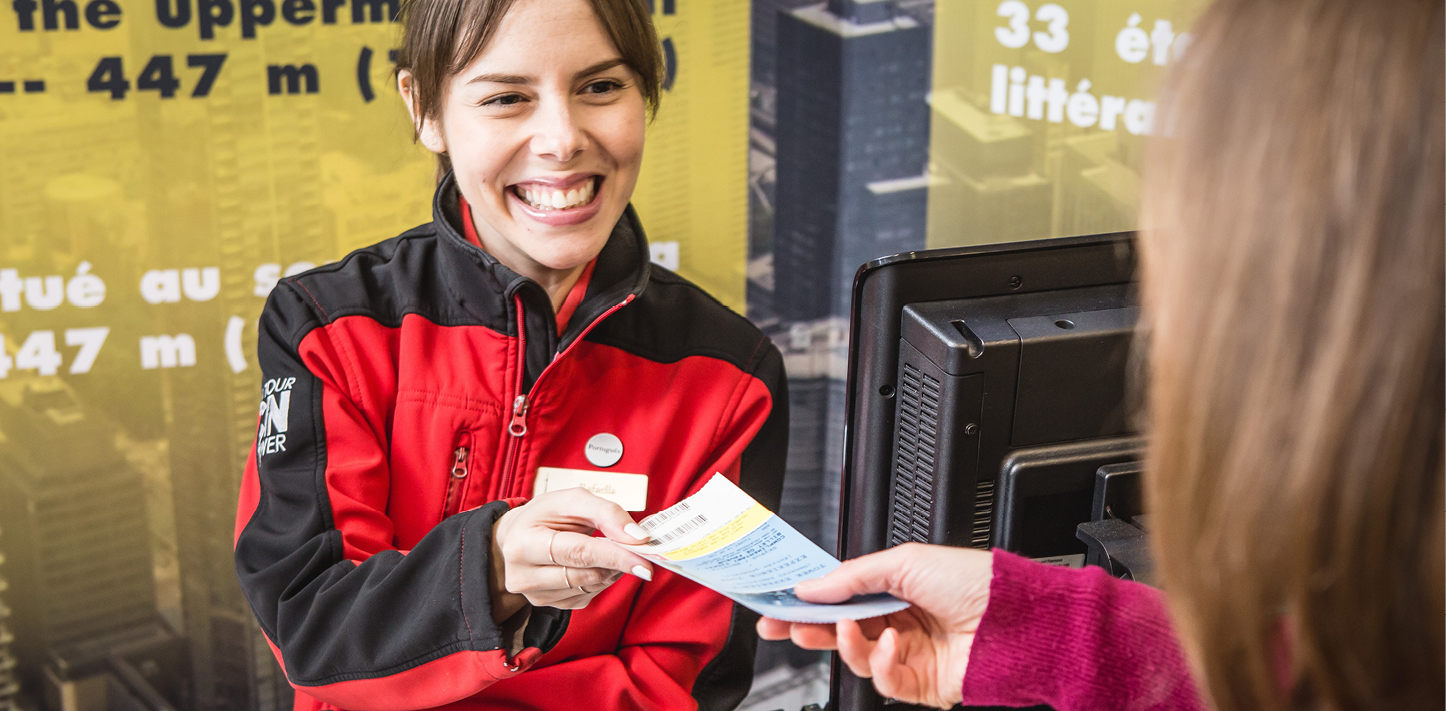 A CN Tower employee smiling while giving a ticket to a visitor