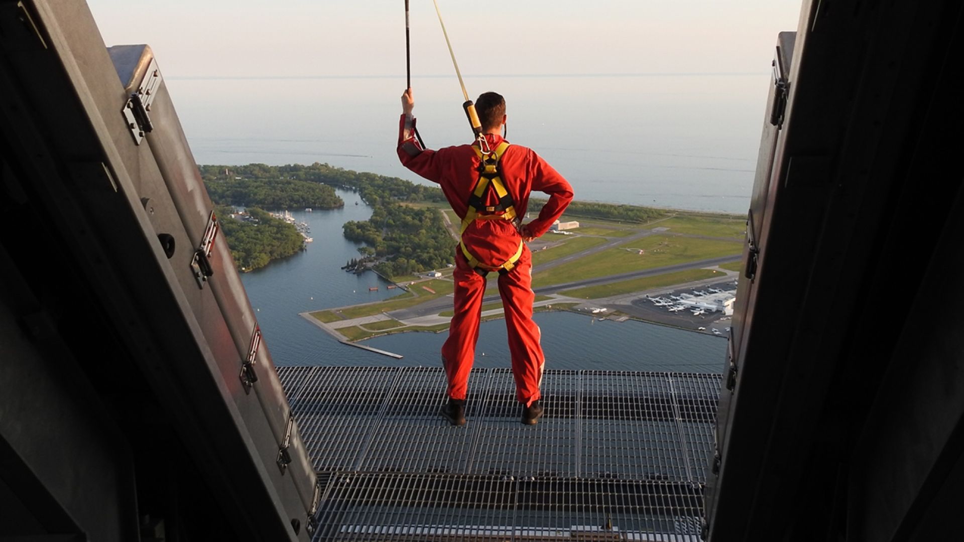 Person standing on the edge of of the Edgewalk wearing a harness and  holding on to the security line