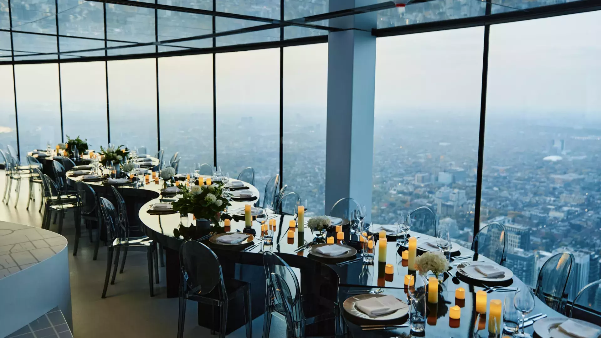 View of a serpentine table set up at the Main Observation Level of the CN Tower. There's a big bouquet of white flowers in the middle, surrounded by empty plates, candles and more flowers.