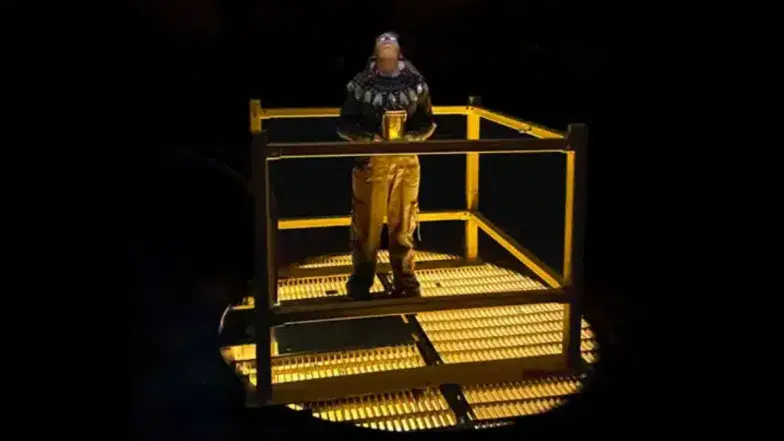 A person looks upward inside the dark, industrial caverns of the CN Tower, surrounded by exposed metal structures and warm lighting.