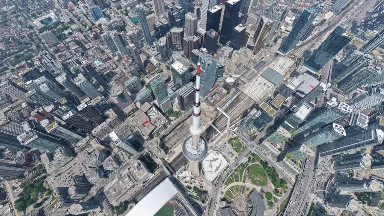 Aerial view of downtown Toronto with the CN Tower at the centre, surrounded by high-rise office and residential buildings. Union Station, the rail corridor, Rogers Centre, and nearby roadways are visible below, highlighting the city's dense urban landscape from above.
