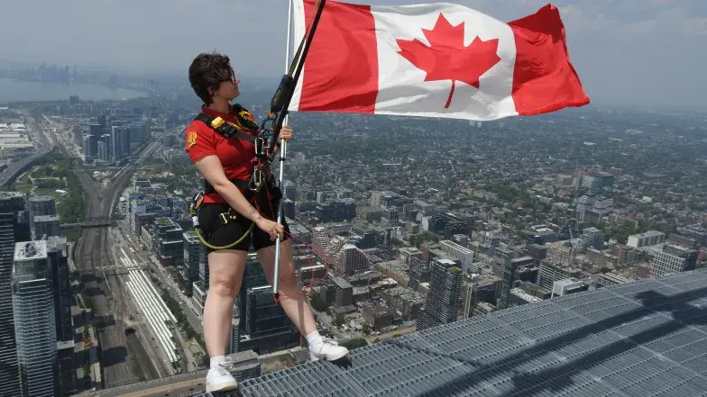 Young person standing on EdgeWalk holding a Canadian flag