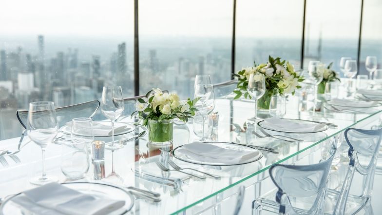 Table and chairs made of clear plexi-glass, elegantly set for dinner positioned along the windows