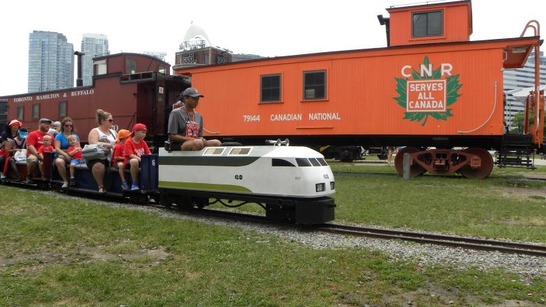 A miniature train, with a group of adults and kids sitting on the train