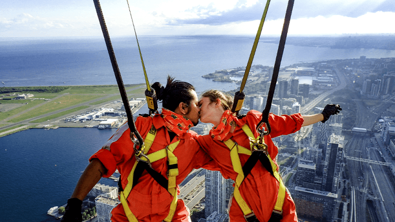 Two people kissing while leaning backwards over the edge. City of Toronto far below.