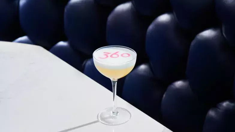 Closeup view of a cocktail in a small coupe glass at 360 Restaurant. The 360 logo is stencilled on the drink.