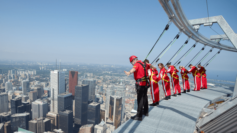 7 people in harnesses leaning forward over the edge. The city below.