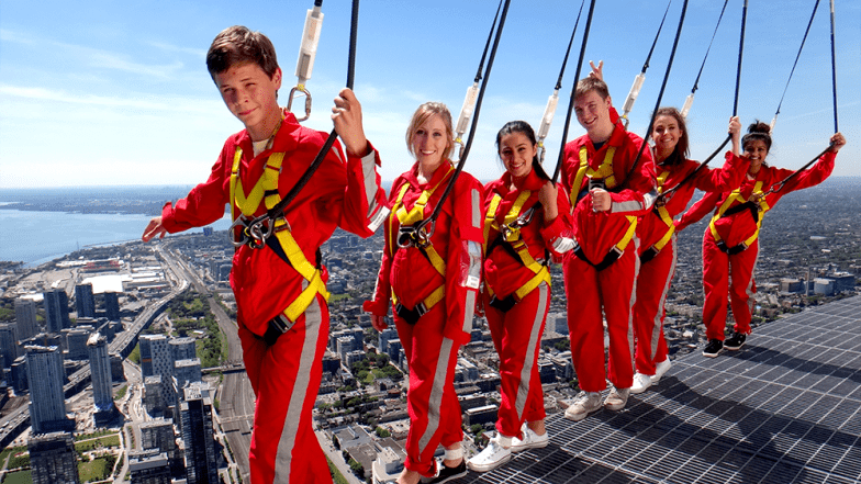 Group of seven people balancing on the edge of the walk. The city below them and clear skies behind them