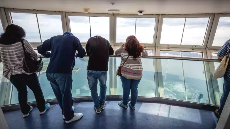 4 people leaning on the railing in the skypod looking down