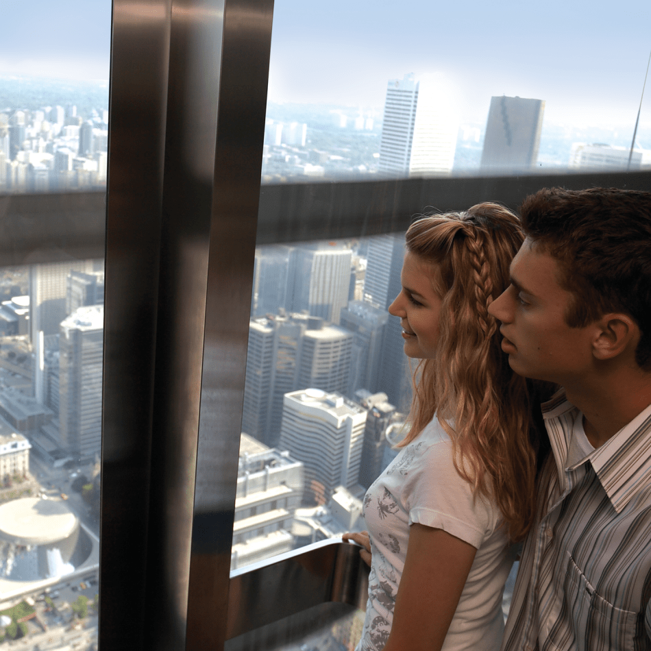 Two people looking through the window of the elevator. The city in the background.