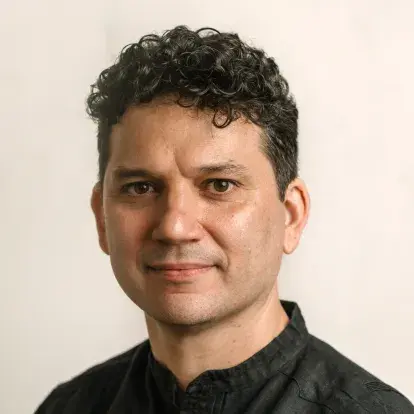 Headshot of Alejandro Basulto facing the camera, with short curly hair, wearing a dark shirt, against a plain light background.