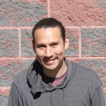 Portrait of Salish artist Dylan Thomas standing in front of a brick wall, smiling.