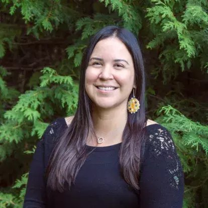 Portrait of Mohawk and Cree artist Katie Longboat standing smiling in front of trees