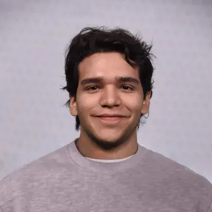 Headshot of Saul Benavides facing the camera against a plain studio background, with short dark hair and a neutral-coloured top.