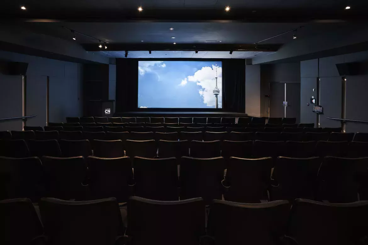 View of cinema from behind the chairs facing the large screen. A podium with CN Tower logo can be seen to the left of the screen. 