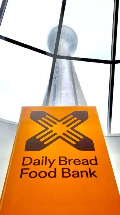daily bread food bank logo on an orange sign, we see the CN Tower in the background through a window