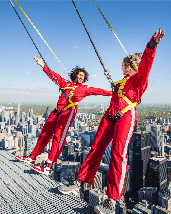 Two people leaning backwards over the edge with the City of Toronto below